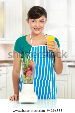 Portrait of a woman posing with a blender and orange juice in her kitchen