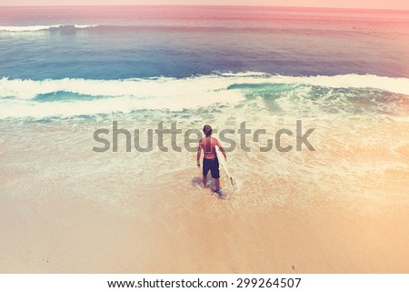 young surfer with a surfer-board goes into the ocean, vintage styly