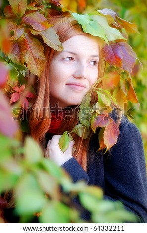 Autumn portrait of a red-haired girl with freckles surrounded by autumn leaves