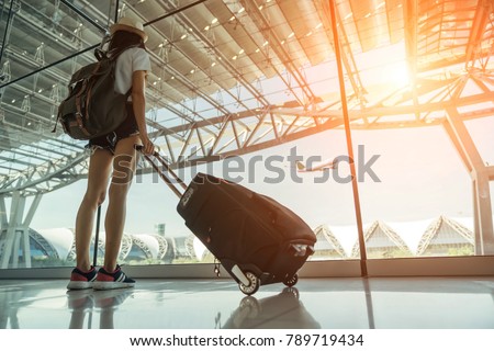 Teen Asian women standing with luggage or suitcase at the window watching aircraft taking off in the international airports in Thailand. Asian girl at International Airport.