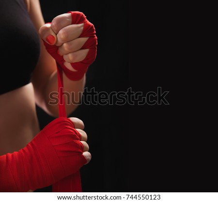 Female boxer is wrapping hands with red boxing wraps. Isolated on black background with copy space. Strong hand and ready for fight, active exercise and sparring. Close up. Women self defense.
