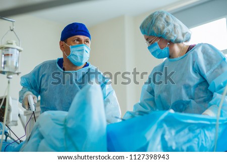 Male surgeon\'s holing the instrument in abdomen of patient. Female assistant help him. The surgeon\'s doing laparoscopic surgery in the operating room. Minimally invasive surgery. Close up
