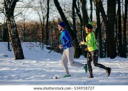 Happy young  couple in winter running and doing  exercises. Runners jogging in snow. Young asian woman fitness model and caucasian man.