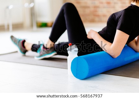 Fitness concept. Close up of woman relaxing after workout on the exercising mat.\
Portrait of Active Tired Woman Using Foam Roller in Light Room.