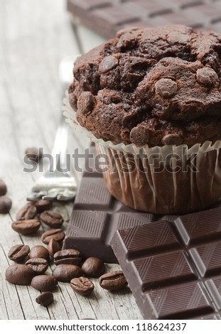Chocolate muffin with dark chocolate pieces and coffee beans on wooden board