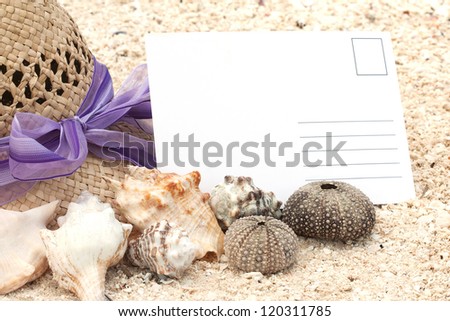 Empty postcard on sand beach among sea shells and a lady hat (manual focus)
