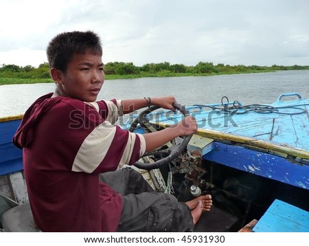 TONLE SAP LAKE, CAMBODIA - CIRCA OCT 2008 : A school boy drives a boat with merely functioning motor for tourists for few dollars to support family, circa October 2008 in Tonle Sap lake, Cambodia.