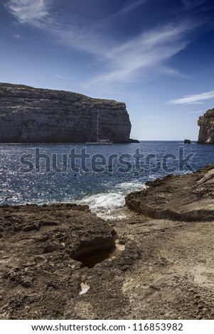 Malta Island, Gozo, Dweira Lagoon, view of a sailing boat and the rocky coastline near the Azure Window Rock