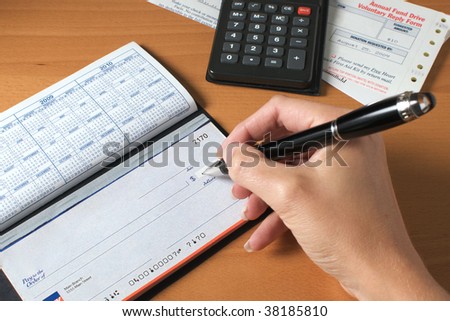 Woman\'s hand writing a check to pay the bills, with calculator and an invoice on the desktop.
