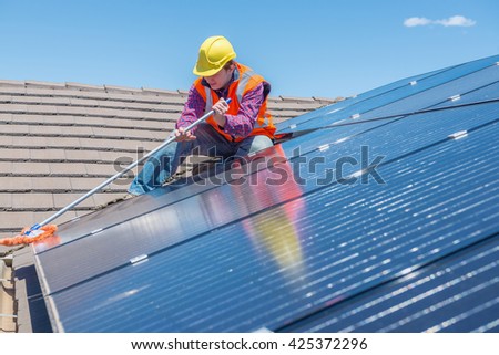 young worker cleaning solar panels on house roof