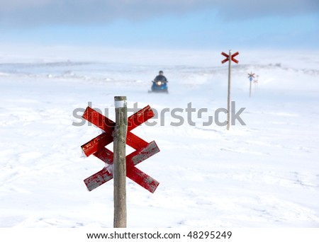 A snowmobile behind a red wooden signpost on a winter day in northern Sweden