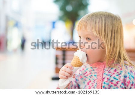 Adorable baby eat ice cream sitting on bench in mall