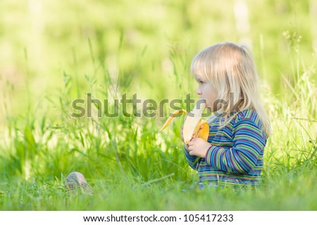 Adorable baby eat banana sitting on grass in park