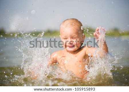 Adorable baby splashing water on lake beach