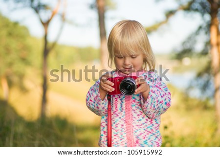Adorable baby shoot compact camera in park on sunset