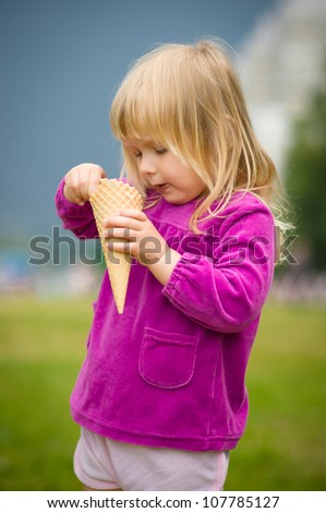 Adorable girl eat ice cream near mall on grass