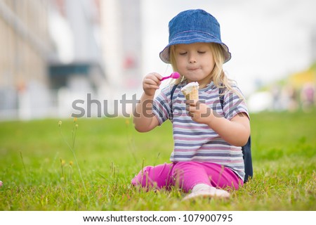 Adorable girl in blue hat eat ice cream sitting on grass