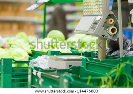 Weighting machine among boxes with vegetables in supermarket