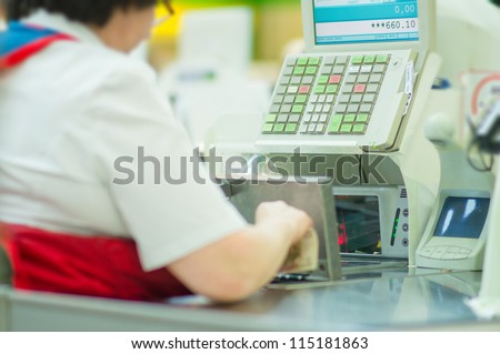 Cash-desk with cashier and terminal in supermarket. Serve customer, holding money in hand