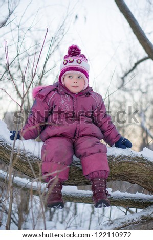 Adorable girl sit on huge tree branch and smile in winter park in evening