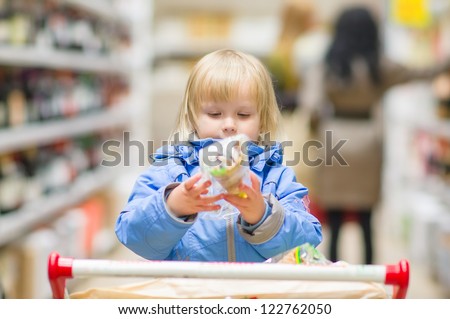 Adorable girl sit on shopping cart with products