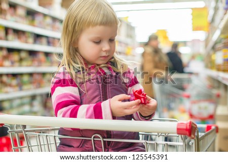 Adorable girl with decoration flower in shopping cart in supermarket