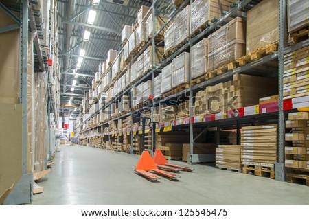 Rows of shelves with huge cardboard boxes and orange storage carts on floor in modern warehouse