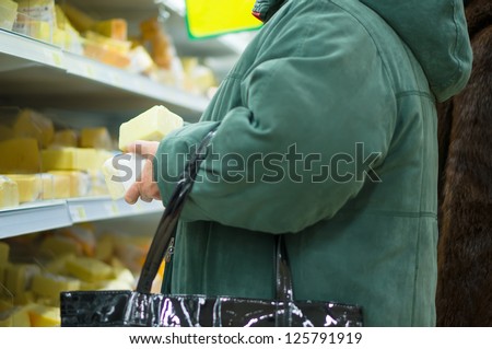 Customer select pieces of cheese on shelves in supermarket