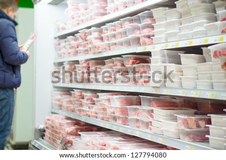 Customer select beef slices in plastic boxes on shelves in supermarket