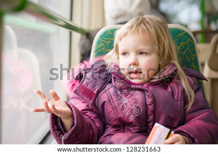 Adorable girl ride on modern city bus. Look to window