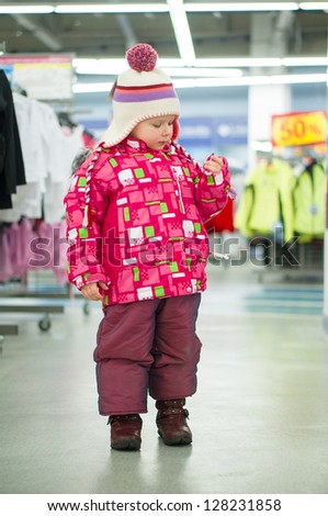 Adorable girl fitting winter jacket and hat in sport store