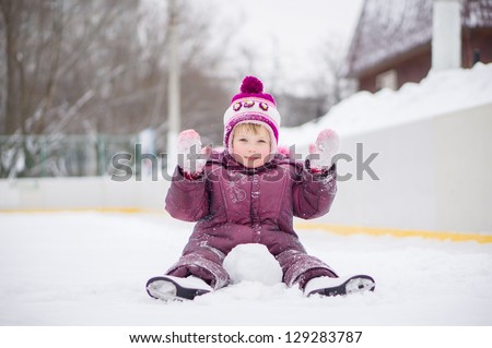 Adorable girl skate on ice rink, seat on ice covered with snow after fall and play with snow