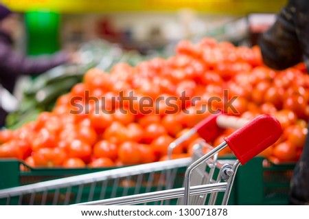 Shopping cart and bunch of tomatoes on boxes in supermarket