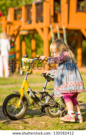 Adorable girl rolling bike with training wheels on playground in park