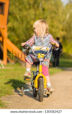 Adorable girl ride on bike with training wheels on playground in park
