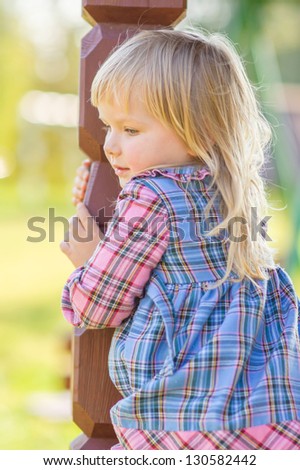 Adorable girl sit on handrails of small house on playground in park
