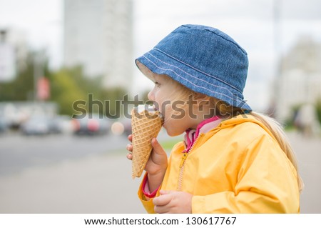 Adorable girl in blue hat eat ice cream on street