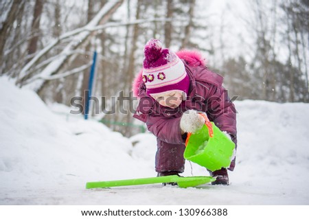 Adorable girl play with snow and water with small shovel and pail in park
