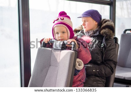 Adorable girl with mother ride on modern city bus in sunny winter day