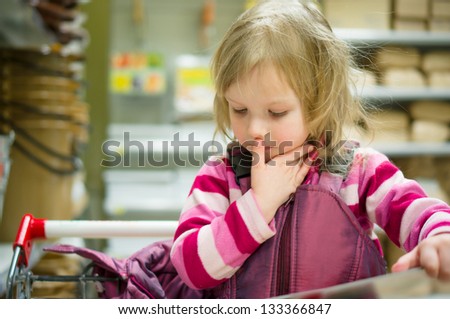Adorable girl in shopping cart select books on shelves in supermarket