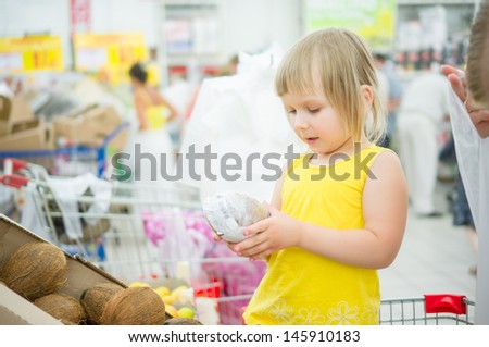 Adorable girl stay in shopping cart and select coconuts