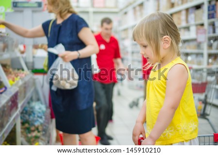 Adorable girl stay in shopping cart and select candies