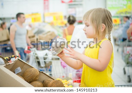 Adorable girl stay in shopping cart and select coconuts