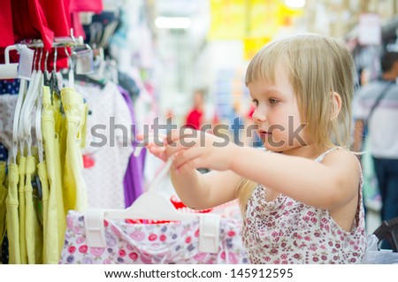 Adorable girl select light dresses in cloth department in supermarket
