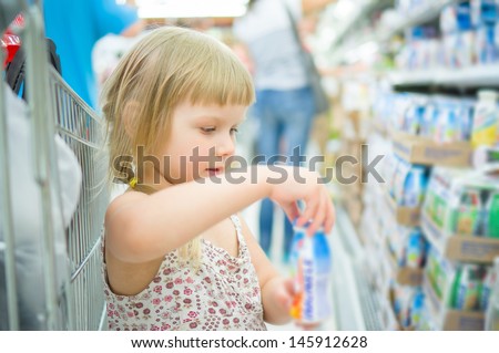 Adorable girl select milk products in supermarket. Holding small bottle