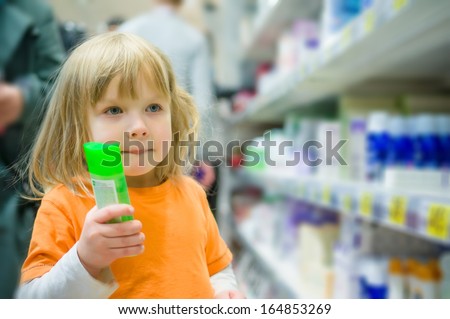 Adorable girl select shampoo bottles in supermarket