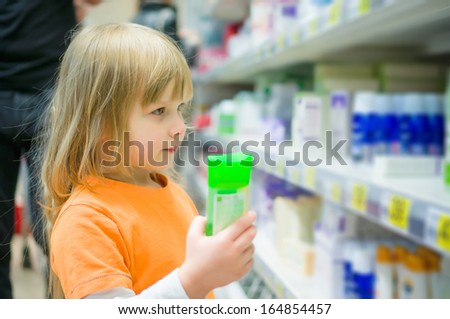 Adorable girl select shampoo bottles in supermarket