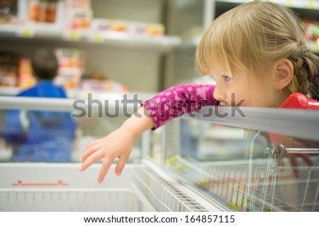 Adorable girl select products at fridge in supermarket