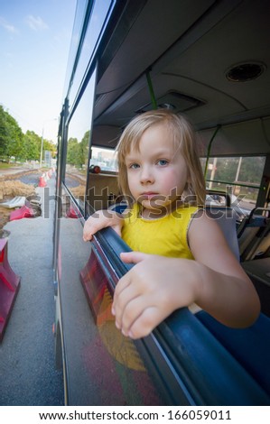 Adorable girl ride by bus and look through open window. Outside shoot