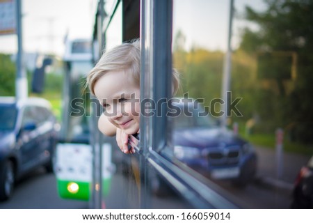 Adorable girl ride by bus and look through open window. Outside shoot